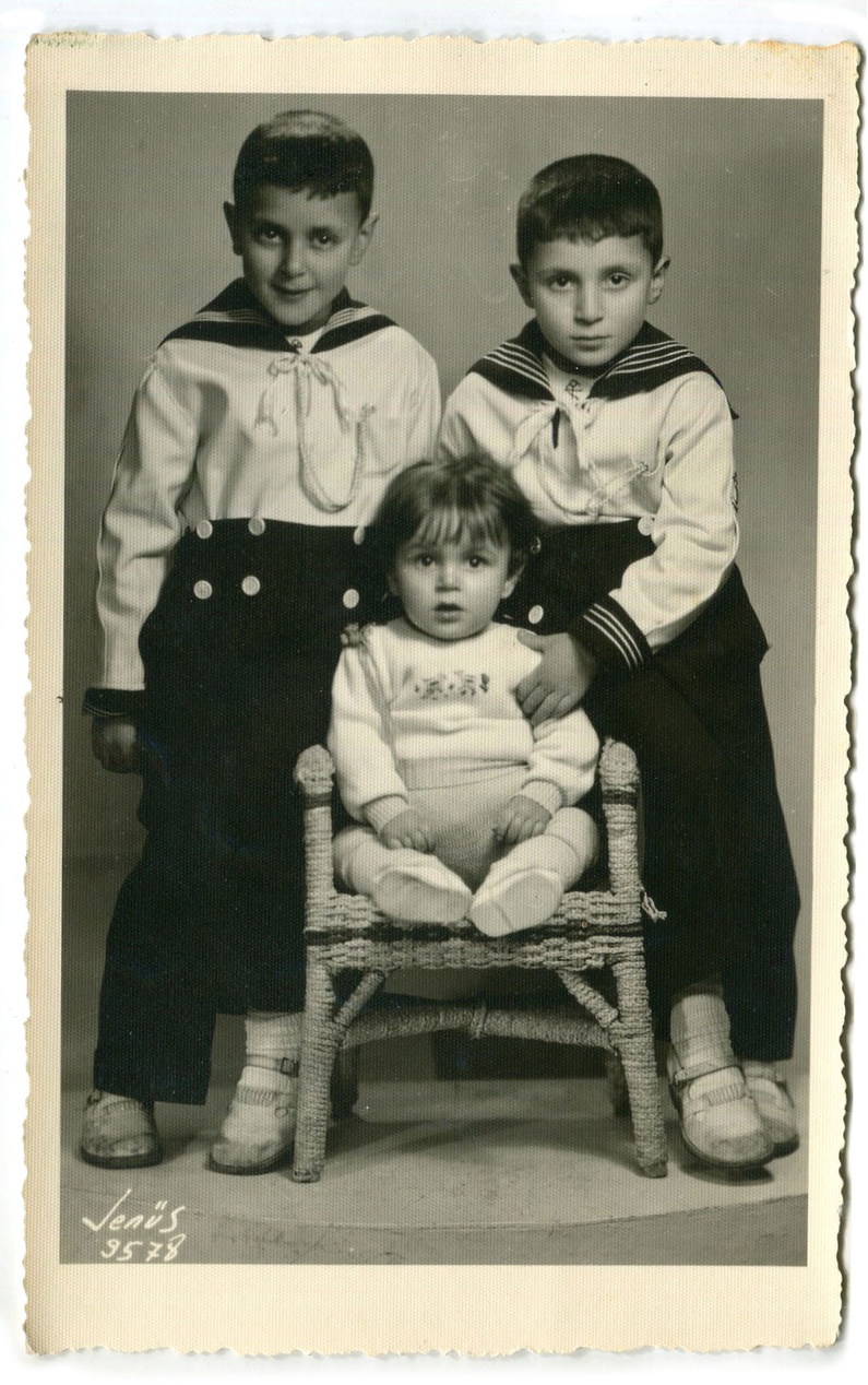 Eine historische Schwarz-Weiß-Aufnahme von drei Kindern in klassischer Kleidung, darunter zwei Jungen in Matrosenanzügen und ein kleines Kind in Weiß.